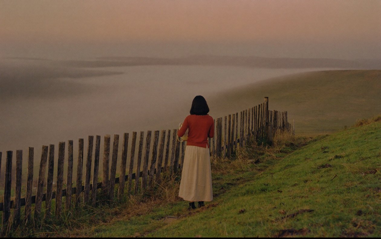 A woman at a fence line at first light, holding an urn