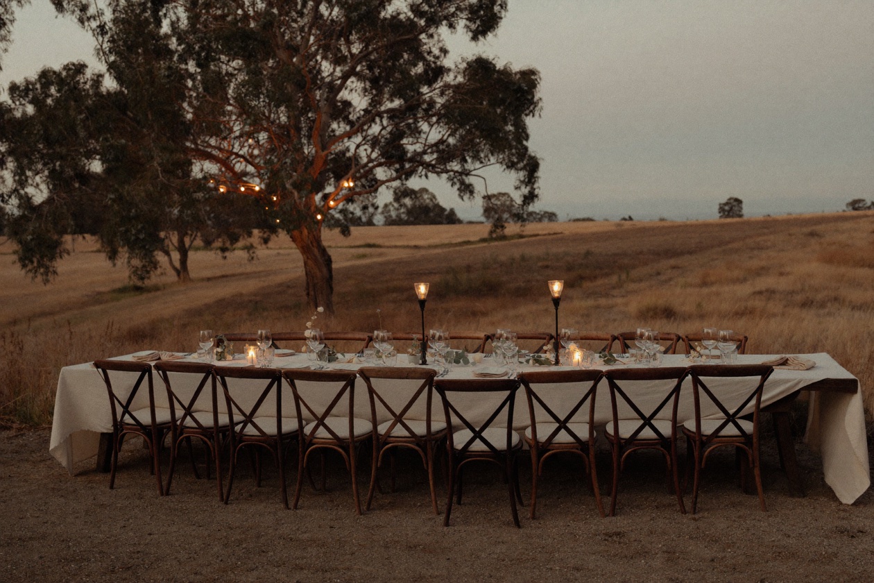 A long table set for a gathering under gum trees at dusk