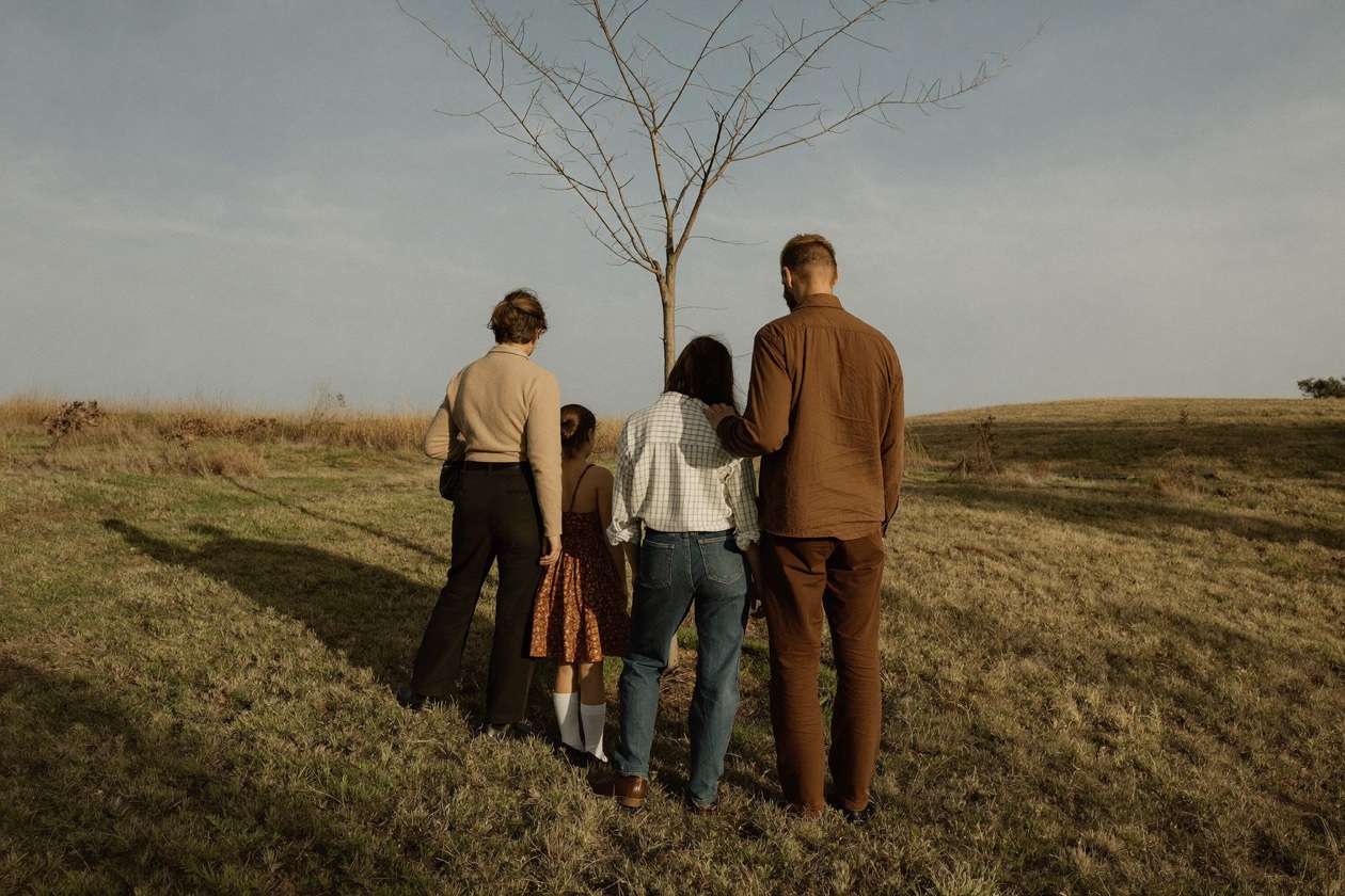 A family gathered around a newly planted tree in a paddock